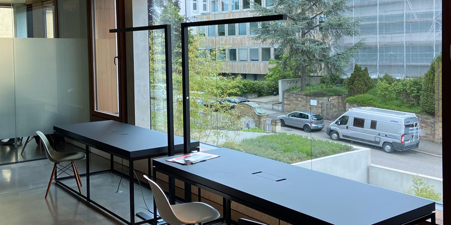 In einem großzügigen Raum mit Fenstern steht ein schwarzer Tisch, auf dem die Econ Office Stehleuchte L platziert ist. Das natürliche Tageslicht strömt durch die Fenster und beleuchtet den Raum.